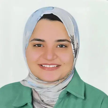 A woman smiles at the camera wearing a grey hijab and a green shirt
