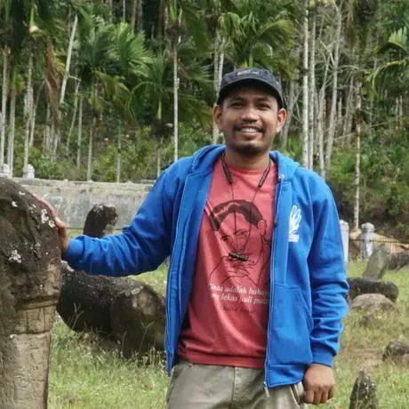A man is smiling wearing a red shirt and blue jacket.