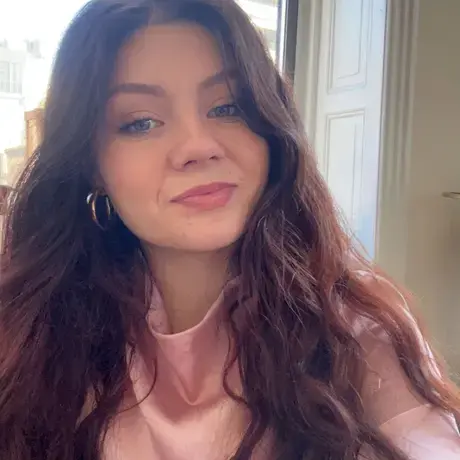 A woman with long brown hair wearing a pink blouse