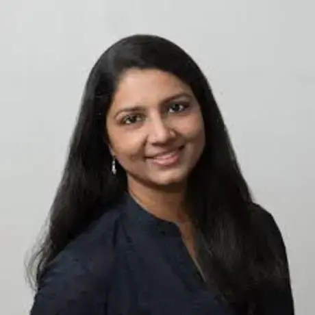 A woman with long dark hair smiles against a neutral background