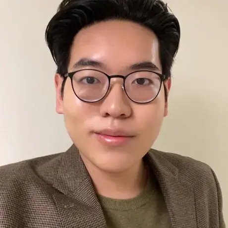 A man with short black hair wearing a green blazer and glasses