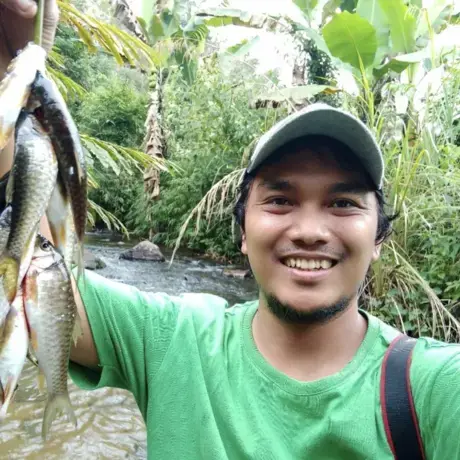 A man wearing a green shirt flashes his teeth as he holds up a bunch of fish in the air.