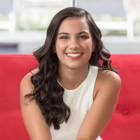 A woman with long dark hair wearing a white top sitting on a red couch