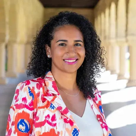 Headshot of a woman with dark curly hair wearing a printed pink and red blazer