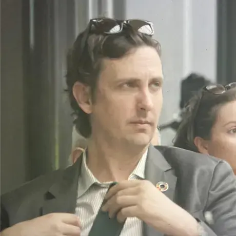 A man wearing a suit and sunglasses on his head looks away from the camera