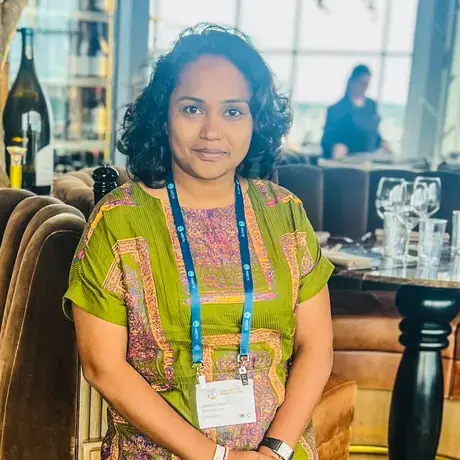 A woman with short dark hair wearing a green embroidered dress and an event lanyard