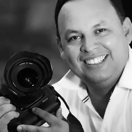 A man gleefully smiles at the camera while holding a camera in his hands.