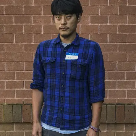 Photo of Go standing against a brick wall wearing a blue button-down
