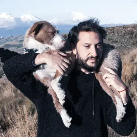 Mijail aA dog is wrapped around Mijail's shoulders against beautiful mountains.