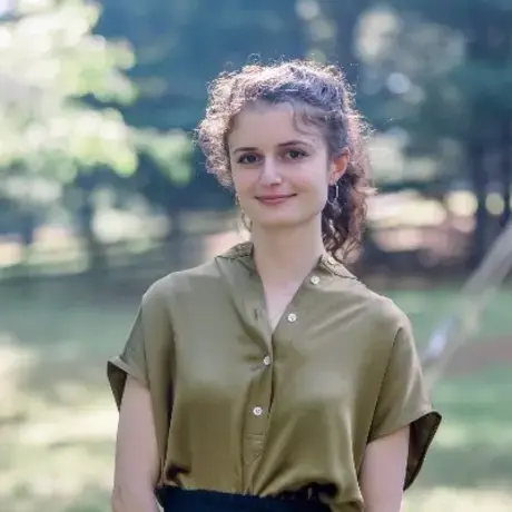 A woman with brown curly hair wearing a green button down shirt standing in an outdoor setting