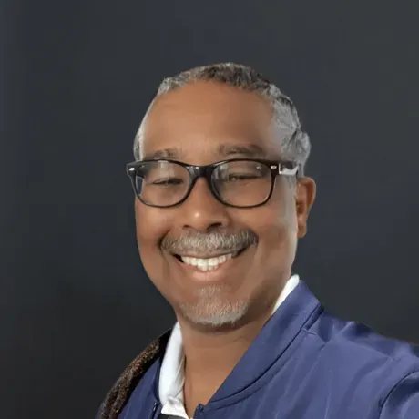 Troy Gordon is a Black man with long grey dreadlocks smiling into the camera