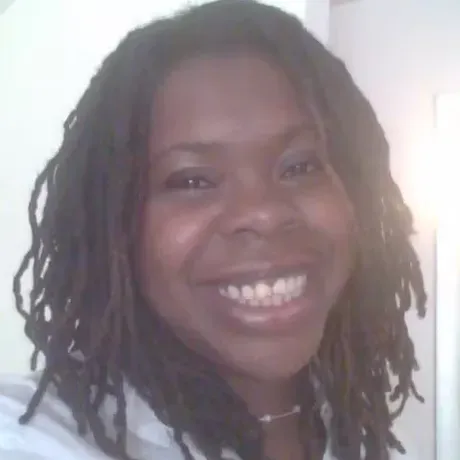A headshot of Aisha Faison, She has locs in her hair and is smiling into the camera.