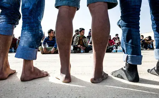 Migrants whose boat was intercepted by the Libyan navy wait to be given shoes before they can be moved to a detention center in Tripoli. Image by Peter Tinti. Libya, 2017.