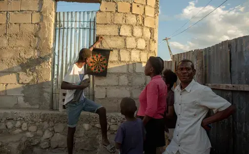 Alisma Robert, right, and children Esaie Robert, 15, Roberson Robert, 7, and Kerline Reobert, 18, standing, enjoy the evening at their home in the Canaan 3 neighborhood of greater Canaan, Haiti, January 7. Thomson Reuters Foundation. Image by Allison Shelley. Haiti, 2019.