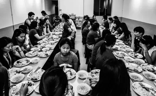 Runaway migrant workers shared a meal inside the kitchen of the shelter. Image by Xyza Bacani. Singapore, 2016. Add this image to a lesson Close to 40 men and women sit around a table and share a meal inside the kitchen of the shelter.