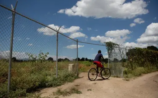 A boy rides past fenced off land in the north of Haiti, April 14, 2015. Much of the area land was appropriated from local farmers to build the nearby Caracol Industrial Park. Image by Allison Shelley. Haiti, 2015.