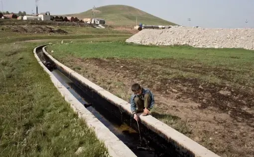 Ezidiar, 9, plays with an oil slick running through the agricultural land below the refinery. Image by Sebastian Meyer. Iraq, 2015.