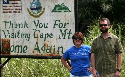 Photojournalist Cheryl Hatch and writer Brian Castner pose for a photograph as they leave Grand Cape Mount county in Liberia on Thursday, Jan. 15, 2015. Hatch is also the adviser to the student newspaper, The Campus, at Allegheny College, and she promised the students she'd take a photo with the shirt somewhere on her trip. Image by Prince Collins. Liberia, 2015. Media file: grandcapemount_9247.jpg