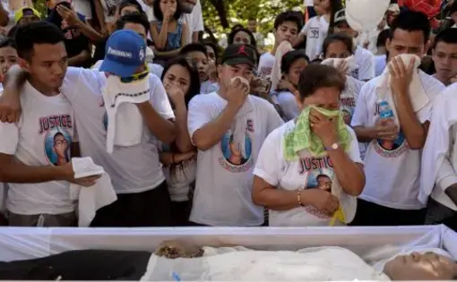 A family and friends of the deceased grieve standing before an open casket.