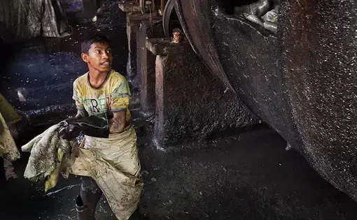 Teenagers work alongside men in some of the most dangerous tannery jobs. Bahadur tosses goat hides into a large drum full of chromium sulfate and other chemicals. Image by Larry C. Price. Bangladesh, 2016.