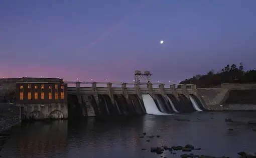 The moon hangs over Lake Hickory as water flows through the gates of the Oxford Hydro Station dam in Conover, North Carolina. The town’s textile industry fled to foreign shores long ago, but a high-tech fabric industry is ascendant. Image by Larry C. Price. United States, 2016.