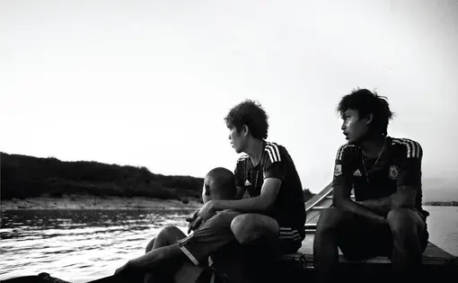 Arkar Min, a former child soldier, works on the Yangon River for a fisherman who is a big fan of the Chelsea soccer club and makes his employees wear the team's jersey as a uniform. Image by Spike Johnson. Burma, 2014. Media file: on-a-boat.jpg