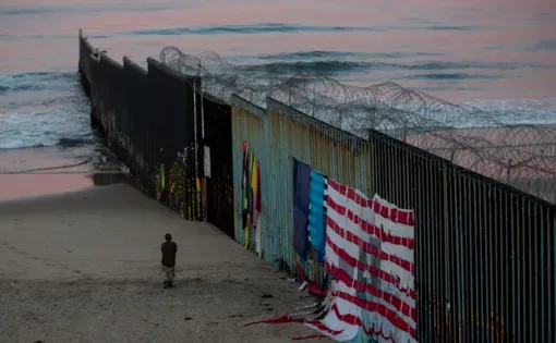 In Tijuana, a man walks at sunrise along the border fence where it meets the Pacific Ocean. Image by Erika Schultz. Mexico, 2019.
