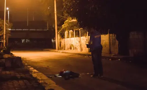 An investigator inspects the body of alias “John Rex,” who was on the village’s drug watch list. Police said he fell from a motorcycle that was driven by an unidentified companion while “John Rex” was shooting at the police. In what police said was an act of self-defense, they fired back at him. Image by Pat Nabong. Philippines, 2017.