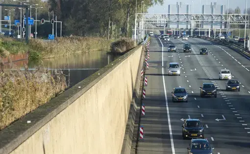 A large wall holds back water, left, as cars on an highway drive under an approaching canal near Rotterdam. Image by Chris Granger. Netherlands, 2019.