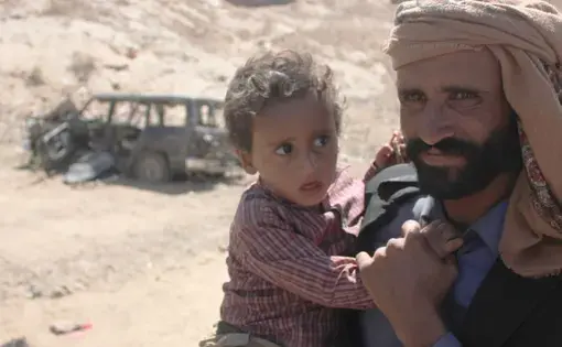 Mabkhout Ali al Ameri stands with his 18-month-old son, Mohammed, in the village of al Ghayil in Yemen’s al Bayda province. Mabkhout’s wife, Fatim Saleh Mohsen, was shot in the back of the head by helicopter gunship fire as she fled with Mohammed in her arms during a U.S. raid. Image courtesy of The Intercept. Yemen, 2017.