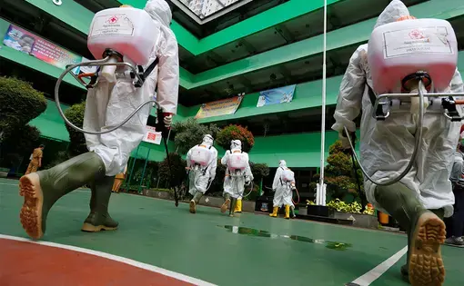 Volunteers from Indonesia's Red Cross prepare to spray disinfectant at a school closed amid the spread of coronavirus (COVID-19) in Jakarta. Image by REUTERS/Willy Kurniawan. Indonesia, 2020. Volunteers from Indonesia's Red Cross prepare to spray disinfectant at a school closed amid the spread of coronavirus (COVID-19) in Jakarta. Image by REUTERS/Willy Kurniawan. Indonesia, 2020.