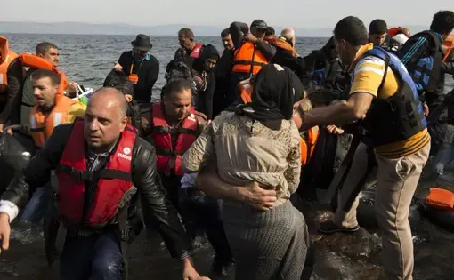Refugees climb out of their dinghy on the shores of Lesbos after having crossed from Turkey, about seven miles away. Image by Tzeli Hadjidimitiou. Greece, 2015.