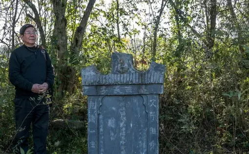 Tan Hecheng at a tombstone put up by Zhou Qun for her husband and three children, who were among the thousands of people killed during the Cultural Revolution in Dao County. Image by Sim Chi Yin. China/VII, 2016.