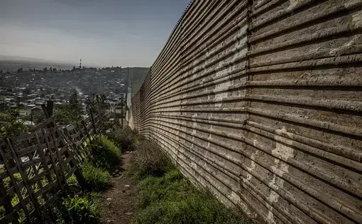 A pattern quickly establishes itself along most of the border fence that separates Baja California, Mexico from California, USA - Mexican urban centers press up against the U.S. border, as if to draw heat from its economic heat, while California cities seem to push back and away from the border, as seen here in Nido de las Águilas (Eagle's Nest) in the east of an expanding Tijuana metropolis. Image by James Whitlow Delano. Mexico, 2017.
