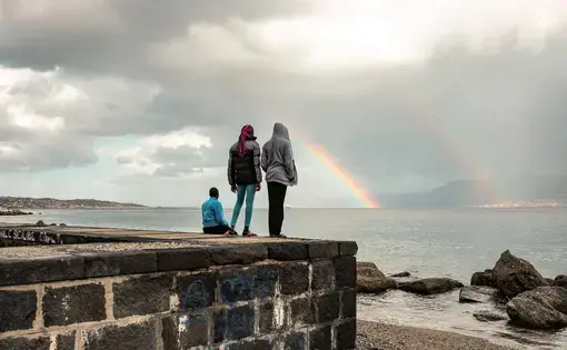 Blessing and two other teen-age Nigerian girls watch a rainbow over the short stretch of water separating Sicily from mainland Italy. Eighty percent of young Nigerian women who cross the Mediterranean are trafficked into sexual exploitation. Image by Ben Taub. Italy, 2017.
