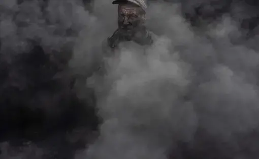 A worker at an outdoor quicklime kiln in the southeastern village of Kosturino, Macedonia. The operation — just one of dozens of prominent sources of air pollution in the country — burns tires for fuel. Image by Larry C. Price. Macedonia, 2018.
