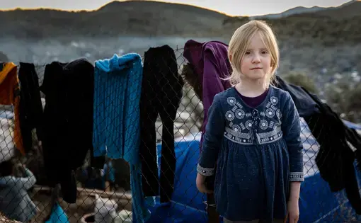 A young girl stands near the laundry she hung to dry in Moria on Lesbos on January 4, 2020. Approximately one-third of the over 20,000 people in Moria are children, and an estimated 1,500 of them are unaccompanied minors. Image by Maranie Staab. Greece, 2020.