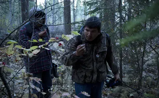 Lucas Shisheesh (right, 21 years old) and Adrian Hookimaw (19) pick wild berries while hiking from a fishing spot on the banks of the Attawapiskat river. Like many other young people I met in Attawapiskat, Lucas spends a great deal of time on the land after being taught by his father how to navigate the wilderness. Image by David Maurice Smith. Canada, 2016.