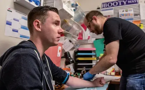 After this test showed Shane Ryan's blood was negative for the AIDS virus, Magnet's nurse practitioner Pierre-Cédric Crouch (background) offered him anti-HIV drugs to prevent infection. Image by Drew Bird for Jon Cohen's "End of AIDS" project. United States, 2015.