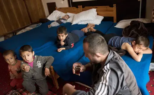 Minhel drinks tea while his children watch television in a hotel in Kastoria, Greece, near the Albanian border. Image by Lynsey Addario. Greece, 2017.
