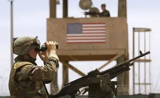 A soldier atop a High Mobility Multipurpose Wheeled Vehicle (HMMWV) surveys the area just outside Camp Delta during a detainee escape exercise in Guantanamo Bay, Cuba. Image by U.S. Navy photo by Journalist Chief (SS) John F. Williams. Cuba, 2003.