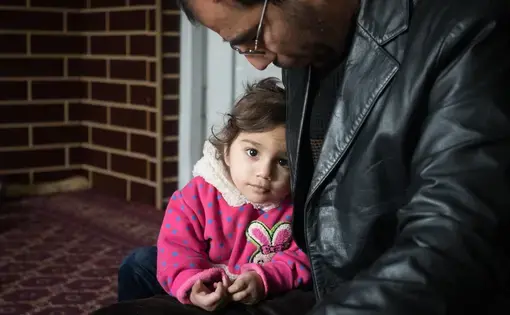 Dr. Wahid Qaderi holds his daughter in his home in Kabul, Afghanistan. His wife, mother, mother-in-law and five children recently crossed by boat from Turkey to Greece, while he stayed behind to try and sell their home. Image by Alexandria Bombach. Afghanistan, 2016. Media file: 1-howwechoose-alexandriabombach.jpg