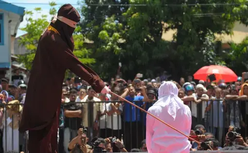 A religious officer canes an Acehnese youth onstage as punishment for dating outside marriage, which is against Sharia, or Islamic law, outside a mosque in Banda Aceh, Aug. 1, 2016. Aceh's landscape is dotted with Saudi influence, but its religious climate is decidedly not. Image from AFP. Indonesia, 2016.