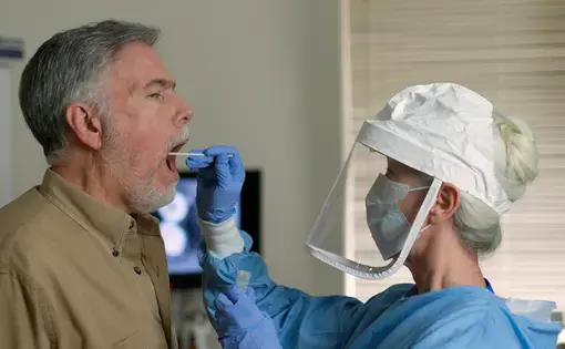 A man being swabbed by a healthcare worker in protective garb to determine if he has contracted the coronavirus. Image by JHDT Productions / Shutterstock. United States, 2020.