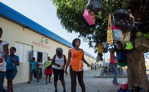 Workers retrieve lunch satchels left hanging in trees outside of a Sae-A Trading Company factory building at the Caracol Industrial Park in the north of Haiti on April 14. Sae-A is the anchor tenant of the $300 million-park, employing about 5,000 workers—still far short of the 60,000 jobs originally projected by 2017. The Clintons were instrumental at nearly every step in its creation. Image by Allison Shelley. Haiti, 2014. Workers retrieve lunch satchels left hanging in trees outside of a Sae-A Trading Company factory building at the Caracol Industrial Park in the north of Haiti on April 14. Sae-A is the anchor tenant of the $300 million-park, employing about 5,000 workers—still far short of the 60,000 jobs originally projected by 2017. The Clintons were instrumental at nearly every step in its creation. Image by Allison Shelley. Haiti, 2014.