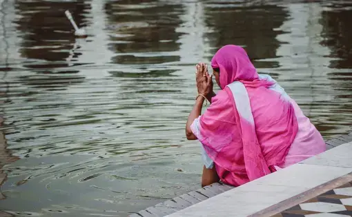 Sikh woman in pink sari dress praying at sacred pool. Image by Gabriela Rosell / Shutterstock. India, undated.