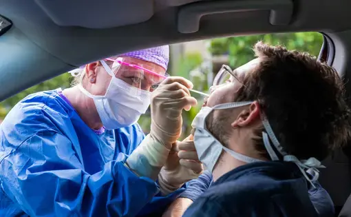 A doctor in a protective suit taking a nasal swab from a person to test for possible coronavirus infection. Image by zstock / Shutterstock. United States, 2020.