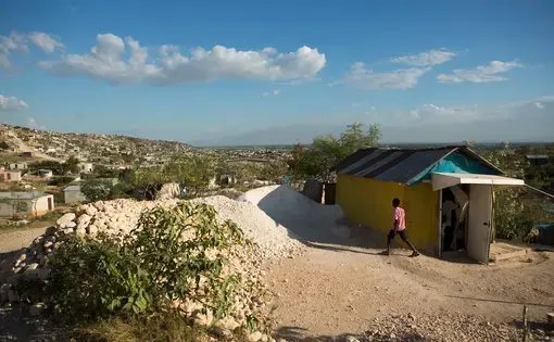 A boy walks past a home in the Canaan I section of the Canaan settlement, just outside of Port-au-Prince, Haiti. Image by Allison Shelley. Haiti, 2018.