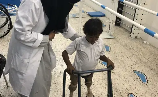 8 year old Imad lost his legs when his home was bombed in 2015.  Samah Mohamed, his prosthetics technician, tries to get him to wear these prosthetics, but they are old, heavy, and don’t bend at the knee. Instead he prefers to scoot around on his hands. He’s one of many children with amputations being treated at the Prosthetic and Physiotherapy Center in Aden. Screenshot from PBS NewsHour.