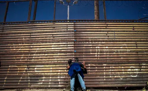 A Honduran migrant observes the displacement of the US military on the other side of the border wall. Image by Simone Dalmasso. Tijuana, 2018.